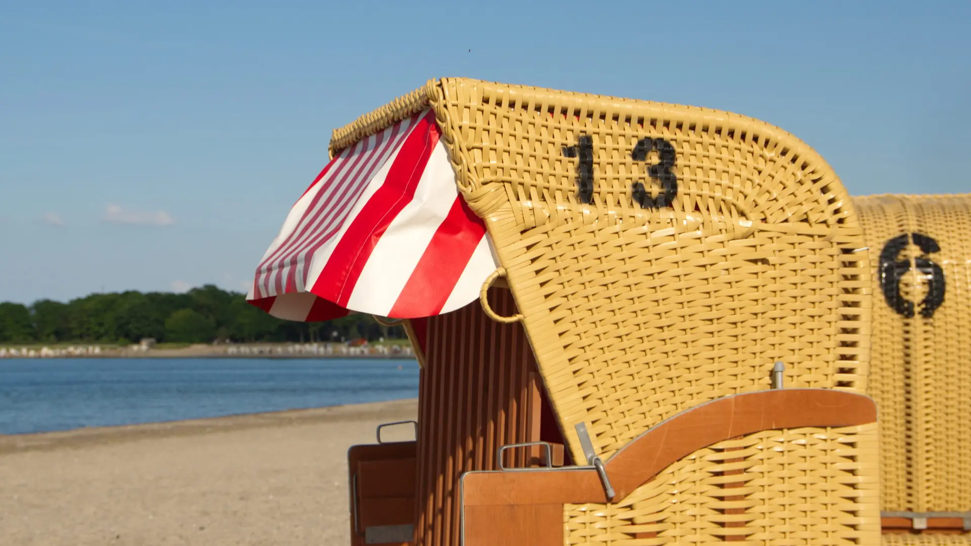 Strandkorb am Meer in der Sonne Nummer 13 drauf Rot Weißes Sonnendach Verschlossen 6 im Hintergrund und das Meer ist zu sehen
